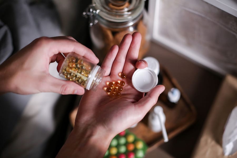Hands tipping amber softgel capsules out of a bottle into an open palm